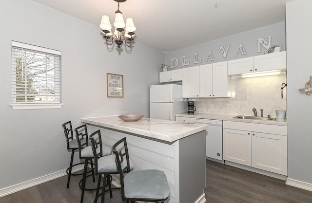 kitchen with dark wood finished floors, decorative backsplash, white cabinets, a sink, and white appliances