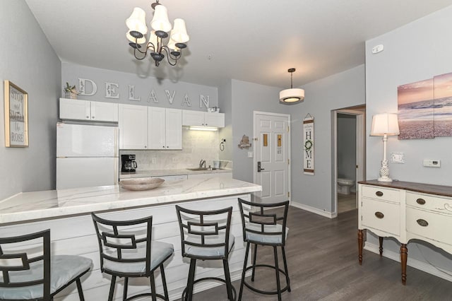 kitchen featuring dark wood-style flooring, a sink, hanging light fixtures, freestanding refrigerator, and decorative backsplash