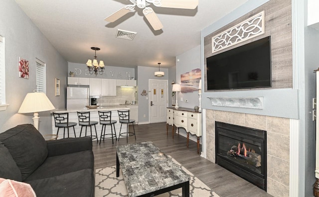 living room with dark wood-style floors, ceiling fan, visible vents, and a tiled fireplace