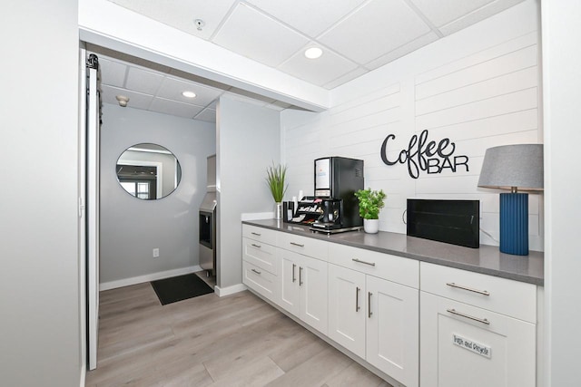 kitchen featuring a drop ceiling, white cabinetry, baseboards, light wood-style floors, and dark countertops