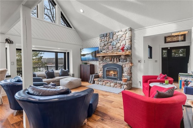 living area with wooden walls, high vaulted ceiling, wood finished floors, and a stone fireplace