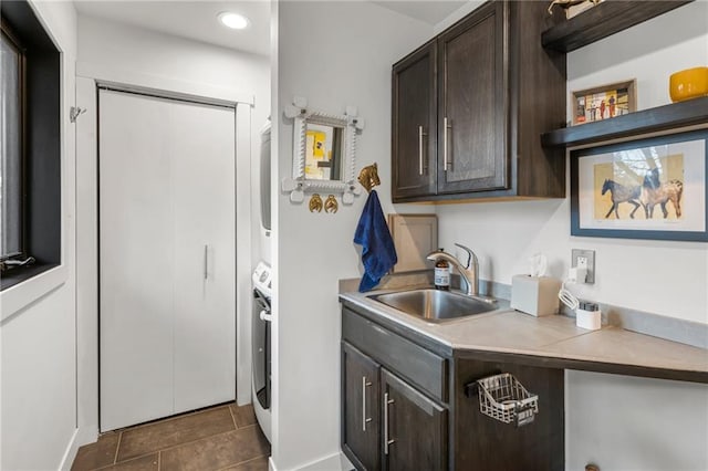 clothes washing area featuring recessed lighting, cabinet space, a sink, stacked washing maching and dryer, and dark tile patterned floors