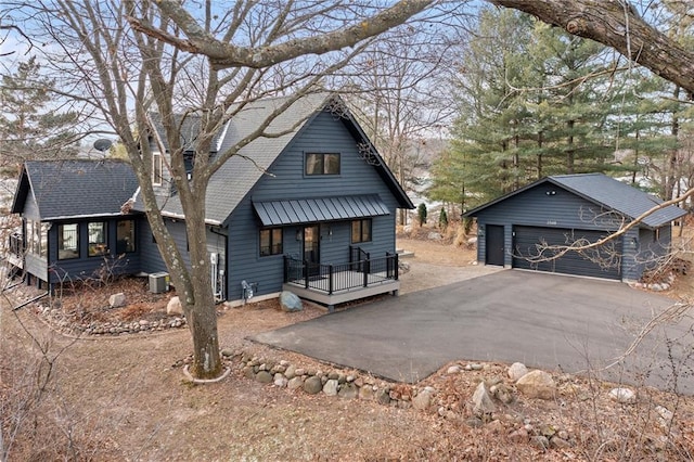 view of front facade featuring central AC unit, a shingled roof, a detached garage, and an outbuilding