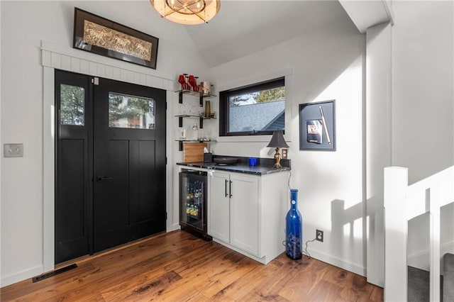 bar with wine cooler, visible vents, vaulted ceiling, a bar, and wood finished floors