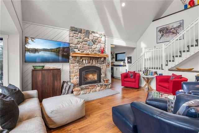 living room with wooden walls, lofted ceiling, stairway, wood finished floors, and a stone fireplace