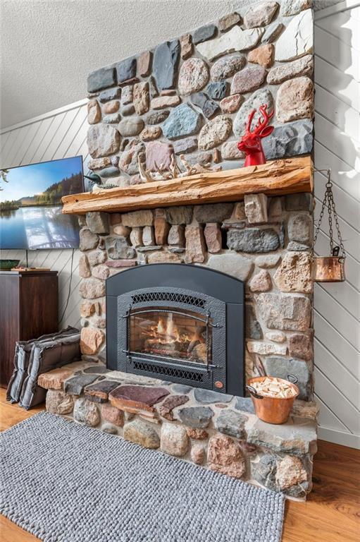 details featuring wood walls, a stone fireplace, a textured ceiling, and wood finished floors