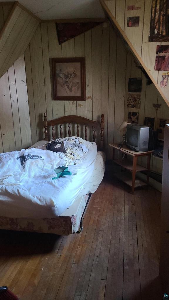 bedroom featuring vaulted ceiling, wood walls, and hardwood / wood-style flooring