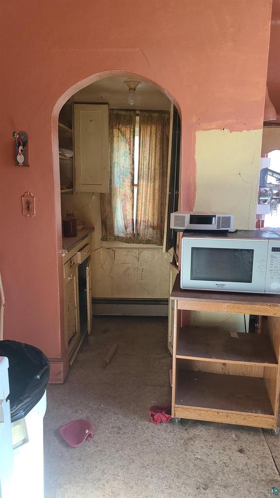 kitchen with a baseboard heating unit, white microwave, and arched walkways