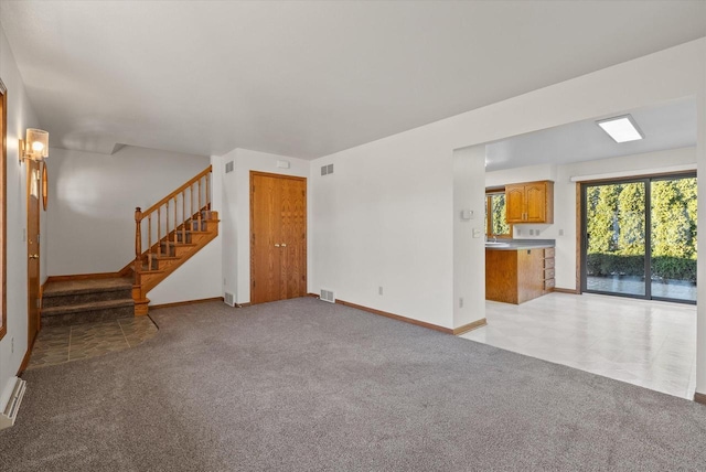 unfurnished living room featuring stairs, visible vents, and light colored carpet