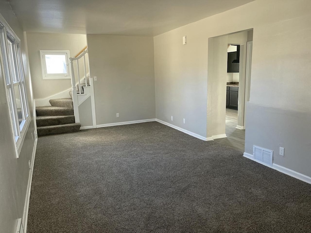 empty room with baseboards, stairs, visible vents, and dark carpet