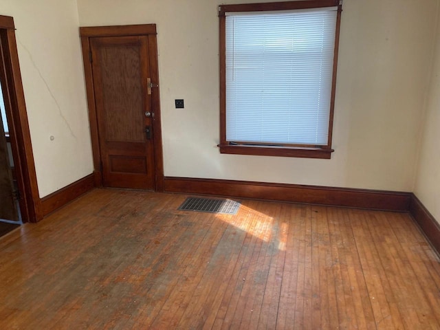 empty room with wood-type flooring, visible vents, and baseboards