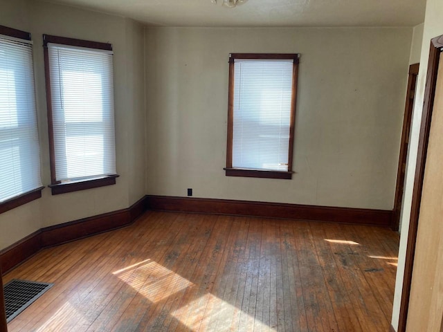 unfurnished room with visible vents, baseboards, and hardwood / wood-style flooring