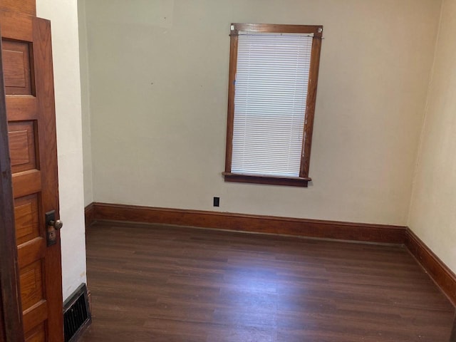 empty room with wood finished floors, visible vents, and baseboards