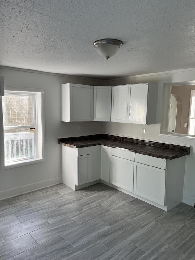 kitchen featuring dark countertops, baseboards, white cabinetry, and a textured ceiling