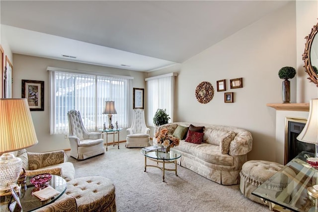 carpeted living area with a glass covered fireplace, visible vents, and lofted ceiling