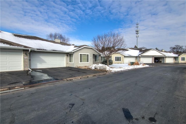 single story home featuring a garage, aphalt driveway, a chimney, and brick siding