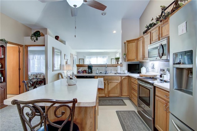 kitchen with a sink, a kitchen island, a kitchen breakfast bar, light countertops, and appliances with stainless steel finishes