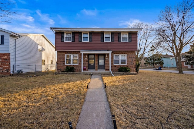 colonial inspired home featuring brick siding, a front yard, and fence