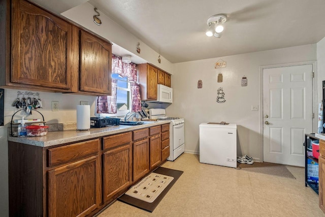 kitchen with a sink, white appliances, brown cabinetry, baseboards, and light floors