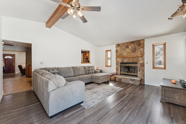 living area with dark wood-style flooring, ceiling fan, lofted ceiling with beams, and a stone fireplace