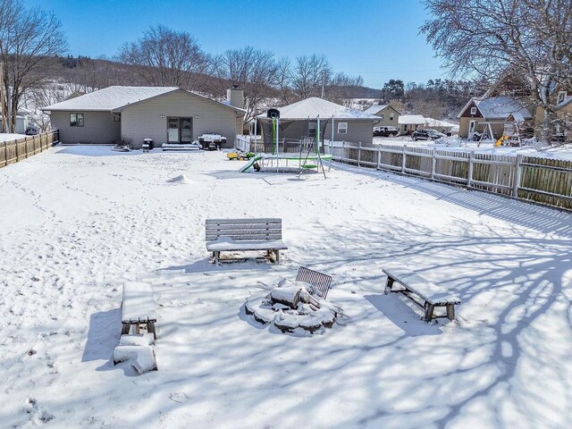 snow covered house featuring a trampoline and a fenced backyard