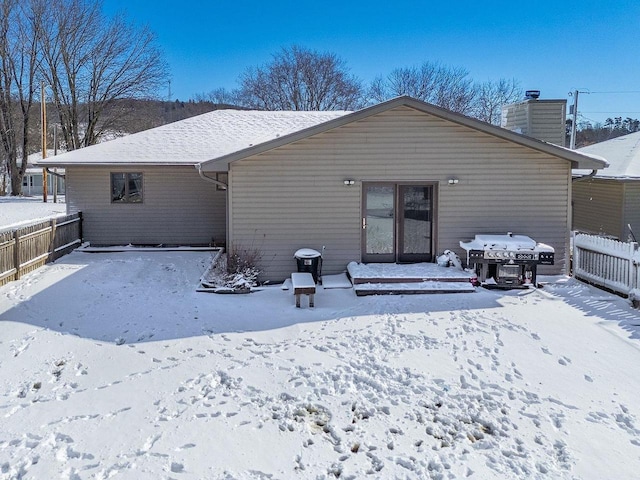 snow covered rear of property featuring a chimney and fence