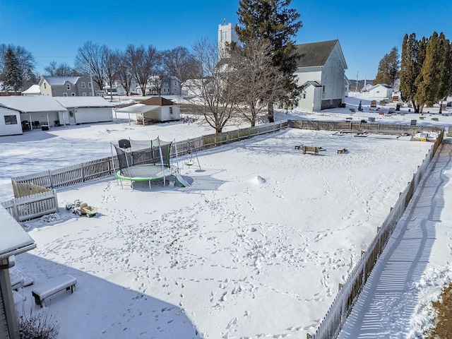 yard layered in snow featuring a trampoline, a fenced backyard, and a residential view