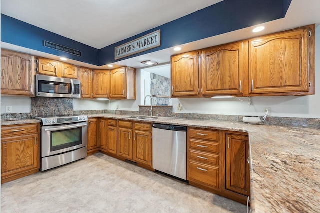 kitchen featuring stainless steel appliances, brown cabinets, a sink, and light stone counters