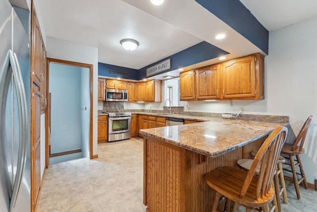 kitchen featuring a breakfast bar, stainless steel appliances, brown cabinetry, a sink, and a peninsula