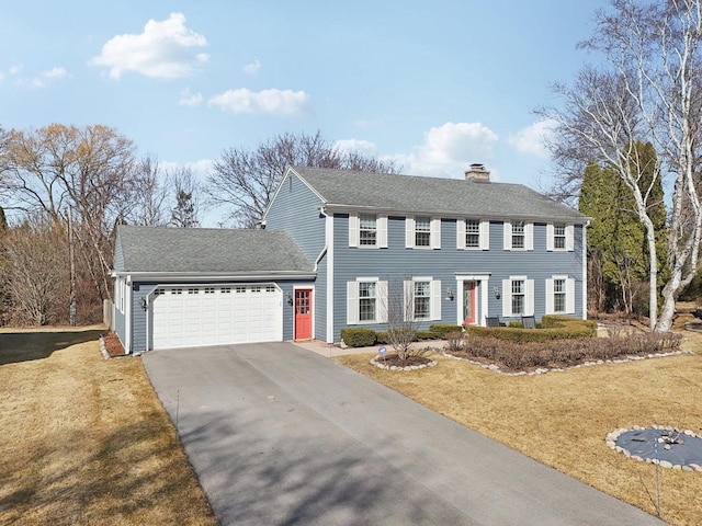 colonial-style house with aphalt driveway, an attached garage, roof with shingles, a chimney, and a front yard