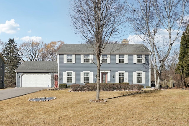 colonial-style house featuring a garage, driveway, a chimney, and a front lawn