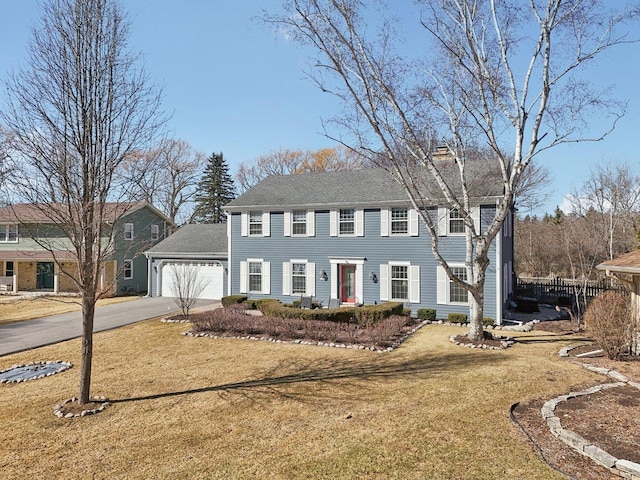 colonial home featuring a garage, concrete driveway, a chimney, fence, and a front lawn