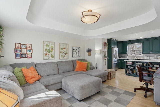 living area featuring a raised ceiling, light wood-style flooring, and recessed lighting