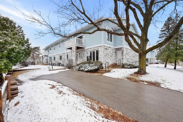 view of snowy exterior featuring stone siding, aphalt driveway, and a balcony