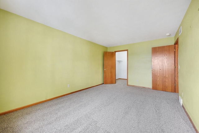 unfurnished bedroom with light carpet, a walk in closet, visible vents, and baseboards