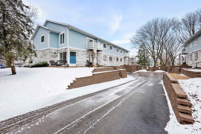 view of front of property with a balcony, stone siding, and aphalt driveway