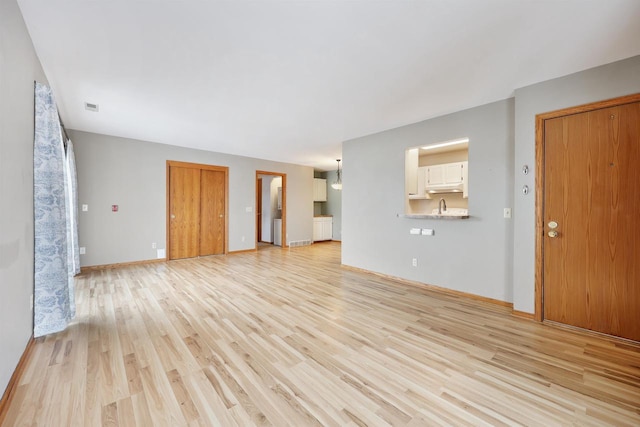 unfurnished living room featuring visible vents, a sink, light wood-style flooring, and baseboards