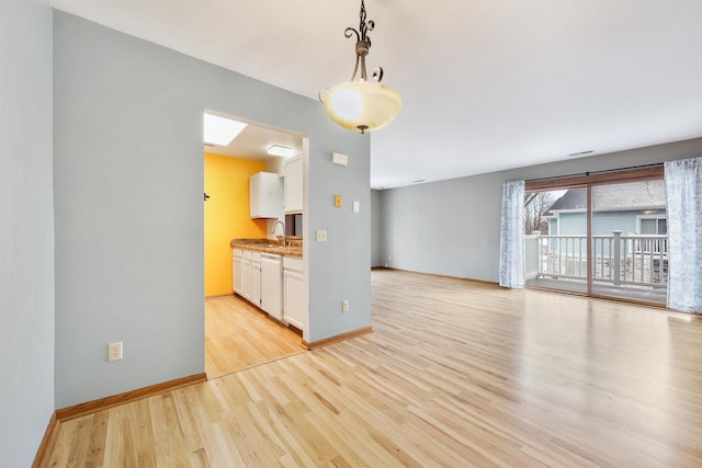 interior space featuring white dishwasher, baseboards, open floor plan, white cabinets, and light wood finished floors