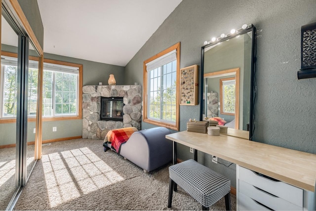 carpeted living room with vaulted ceiling, a textured wall, a stone fireplace, and baseboards