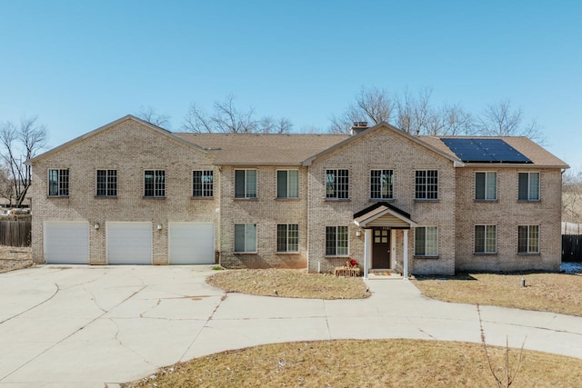 view of front facade with concrete driveway, brick siding, fence, and solar panels