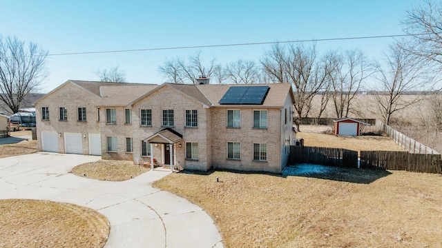 colonial house with an attached garage, fence, driveway, roof mounted solar panels, and a chimney