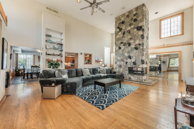 living room with a ceiling fan, visible vents, a stone fireplace, and wood finished floors