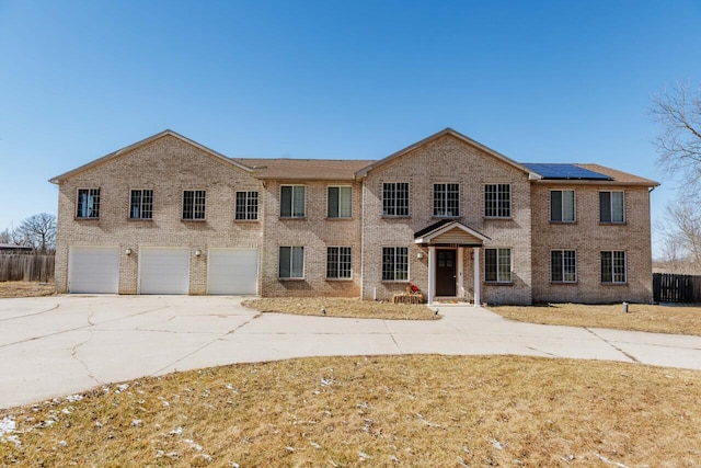 view of front of home featuring a garage, solar panels, brick siding, fence, and driveway