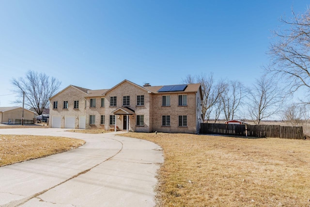 colonial house featuring driveway, a garage, a chimney, fence, and roof mounted solar panels