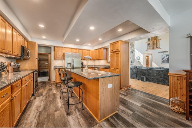 kitchen with appliances with stainless steel finishes, a breakfast bar, a kitchen island, and dark wood-style floors