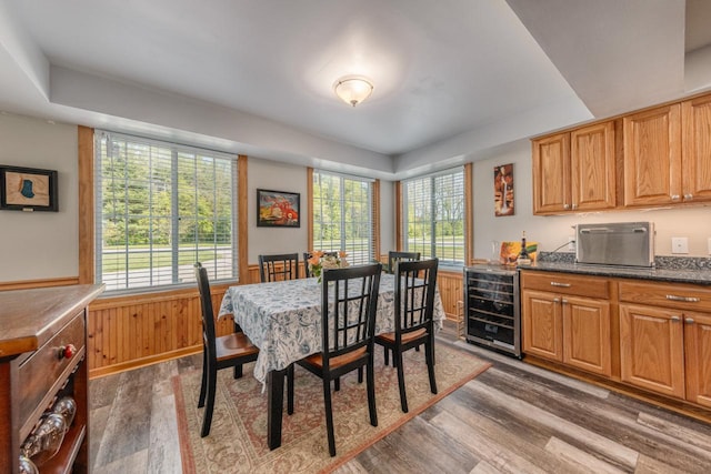 dining space with dark wood-style floors, beverage cooler, a tray ceiling, and a wainscoted wall