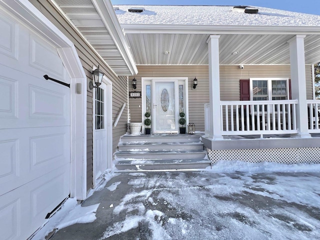 snow covered property entrance featuring a garage and covered porch