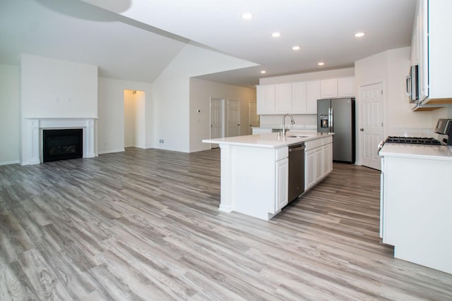 kitchen featuring stainless steel appliances, a sink, white cabinetry, light countertops, and a center island with sink