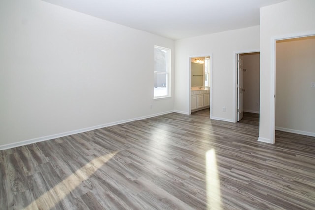 unfurnished bedroom with a walk in closet, ensuite bathroom, baseboards, and wood finished floors