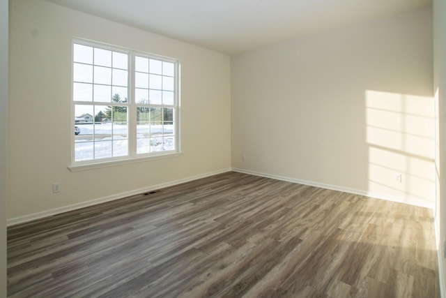 unfurnished room with dark wood-style floors, visible vents, and baseboards